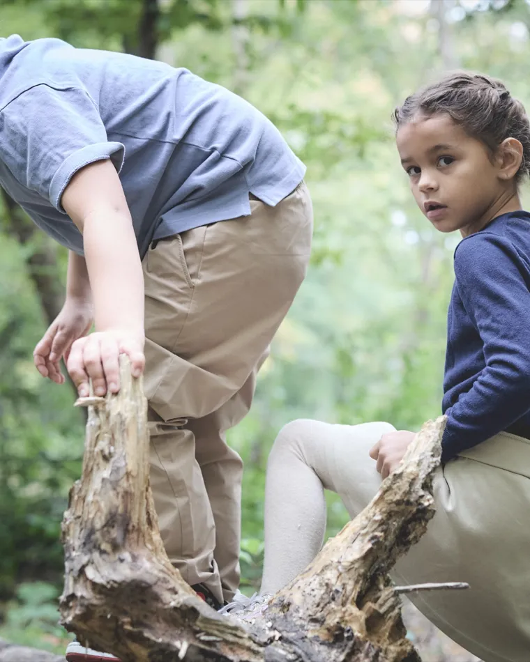 Two students balancing along a fallen log in the woods