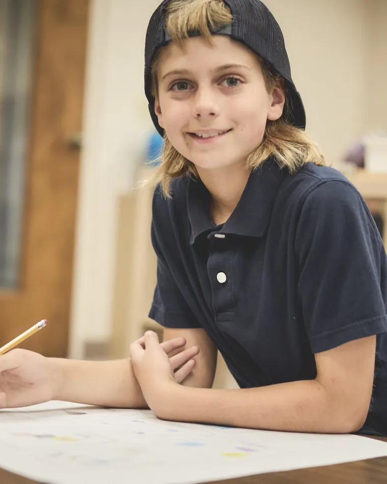 A smiling student working at a classroom table with a pencil in hand