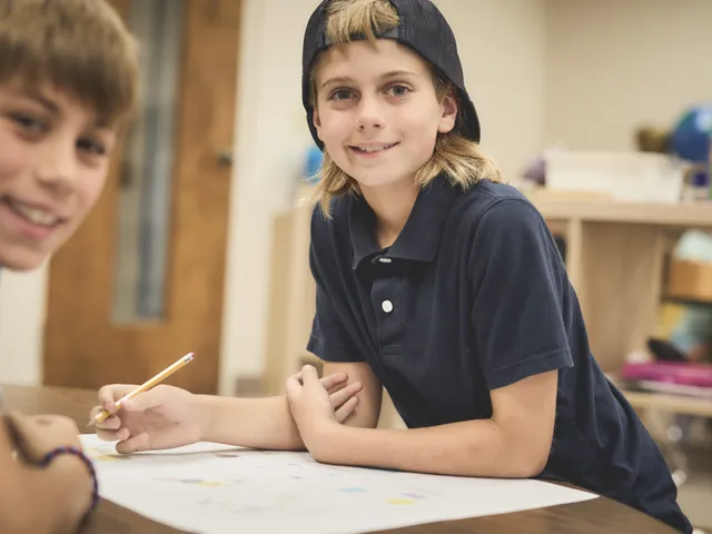 An upper elementary student smiling while writing at a classroom table