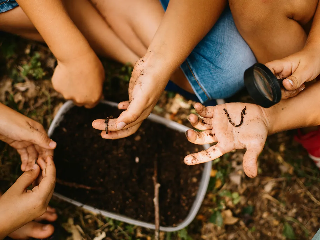 Children exploring soil together with a magnifying glass during a hands-on outdoor lesson